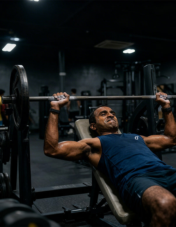 Indian male athlete mid bench press rep with visible sweat, representing electrolyte loss during gym workouts